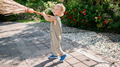 funny kid with broom on walkway in garden in sunlight