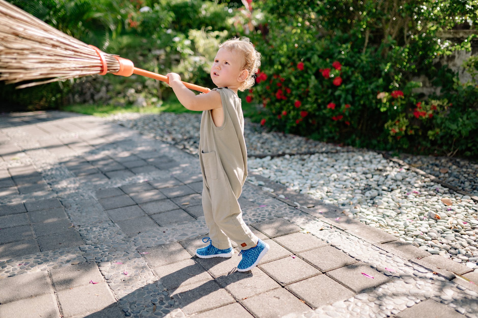 funny kid with broom on walkway in garden in sunlight