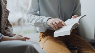 man in white dress shirt and brown pants sitting on white chair reading book